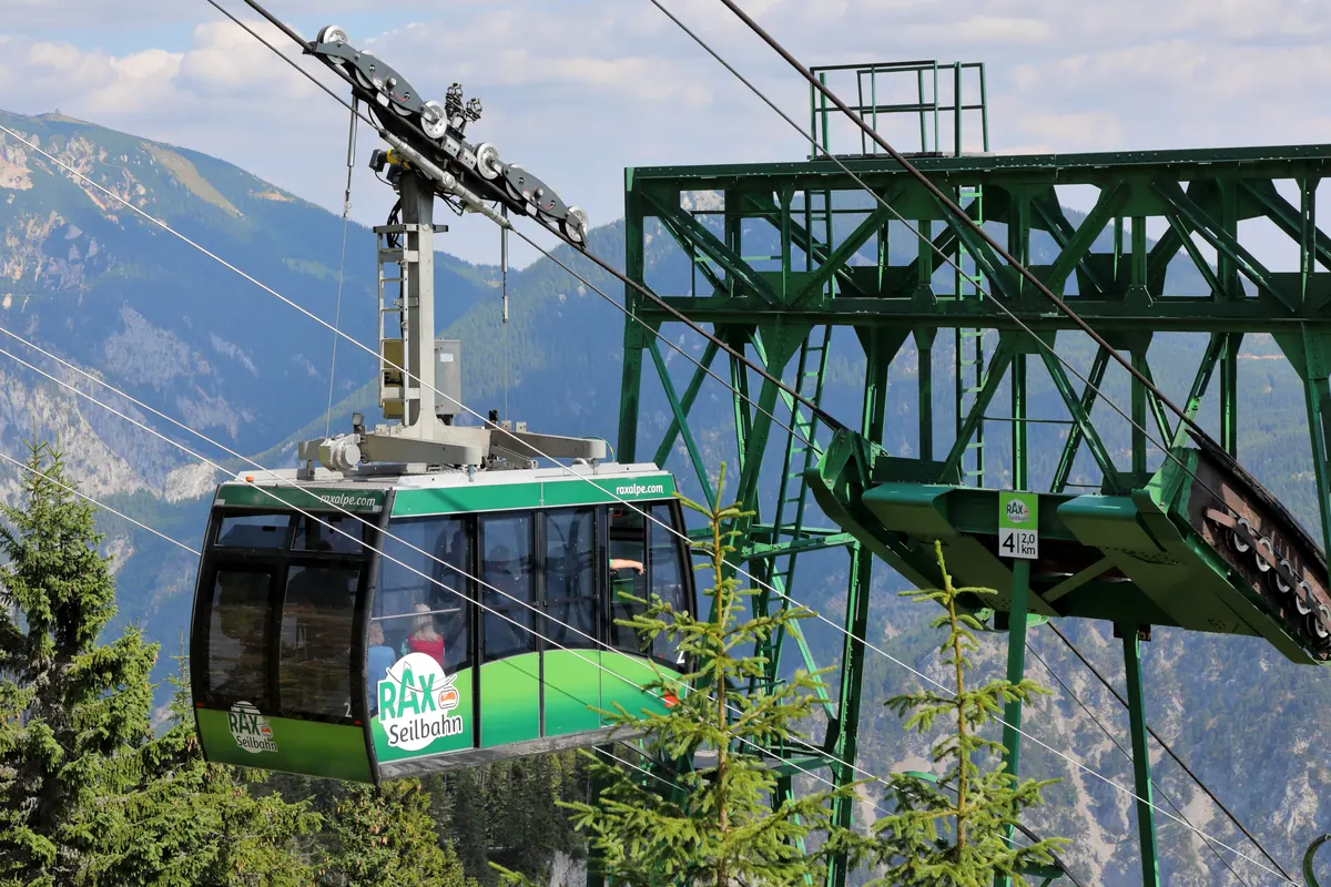 Today's green Raxseilbahn cabin arriving at a steel pylon, mountains behind.